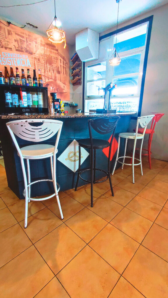 Taburetes y barra de la cafetería del asador Edan, al fondo grifos de cerveza y cafetera