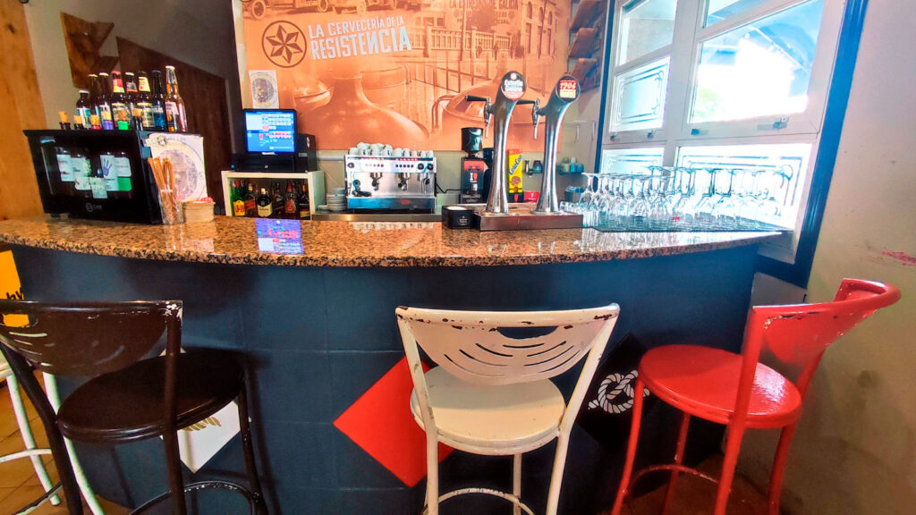 Taburetes y barra de la cafetería del asador Edan, al fondo grifos de cerveza y cafetera