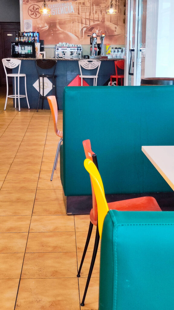 en primer plano mesas de la zona de cafetería y al fondo la barra del bar en asador Edan